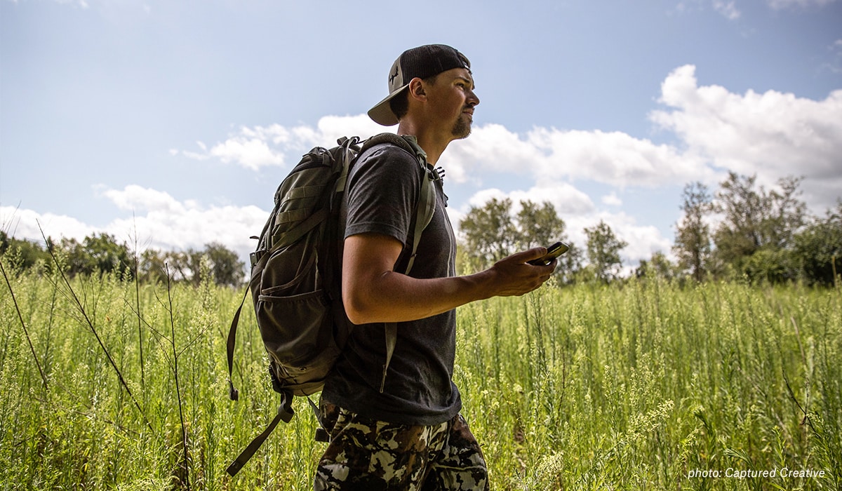 Mark Kenyon walks though a field with his onX Hunt App on his phone.