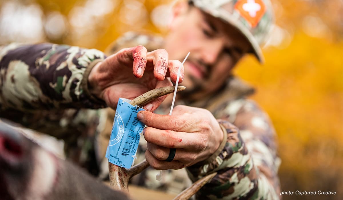 A man putting a tag on a deer he shot while hunting in the Midwest.