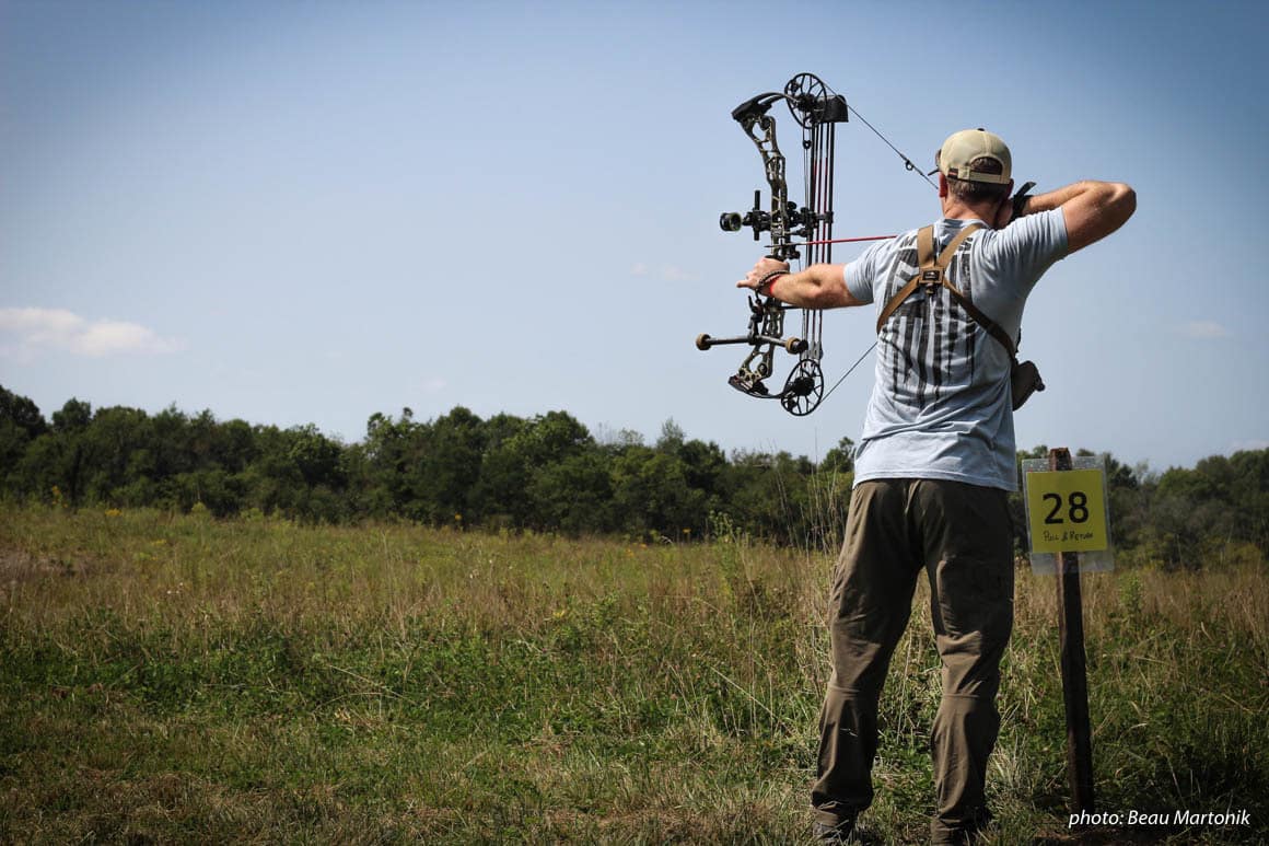 Man practicing compound bow in field.