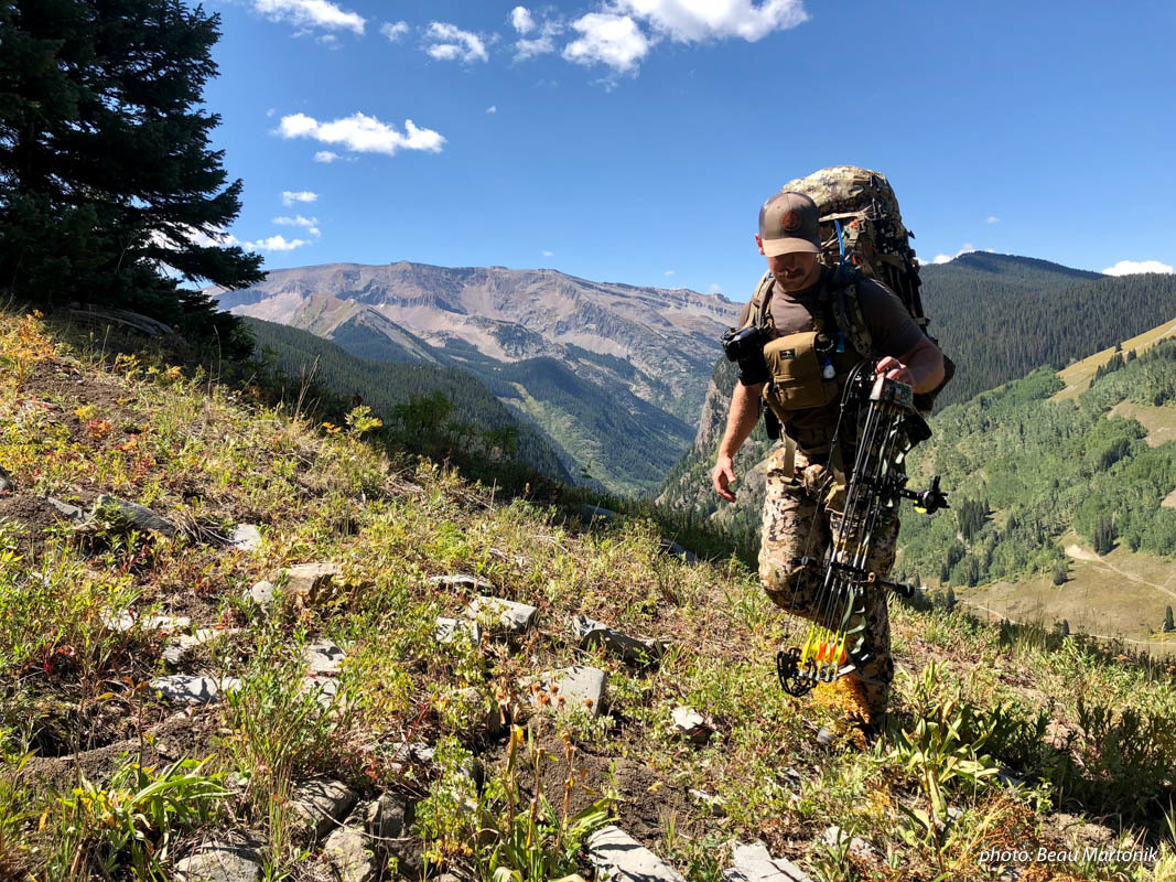 Man bowhunting in mountains with pack, bow and camouflage.