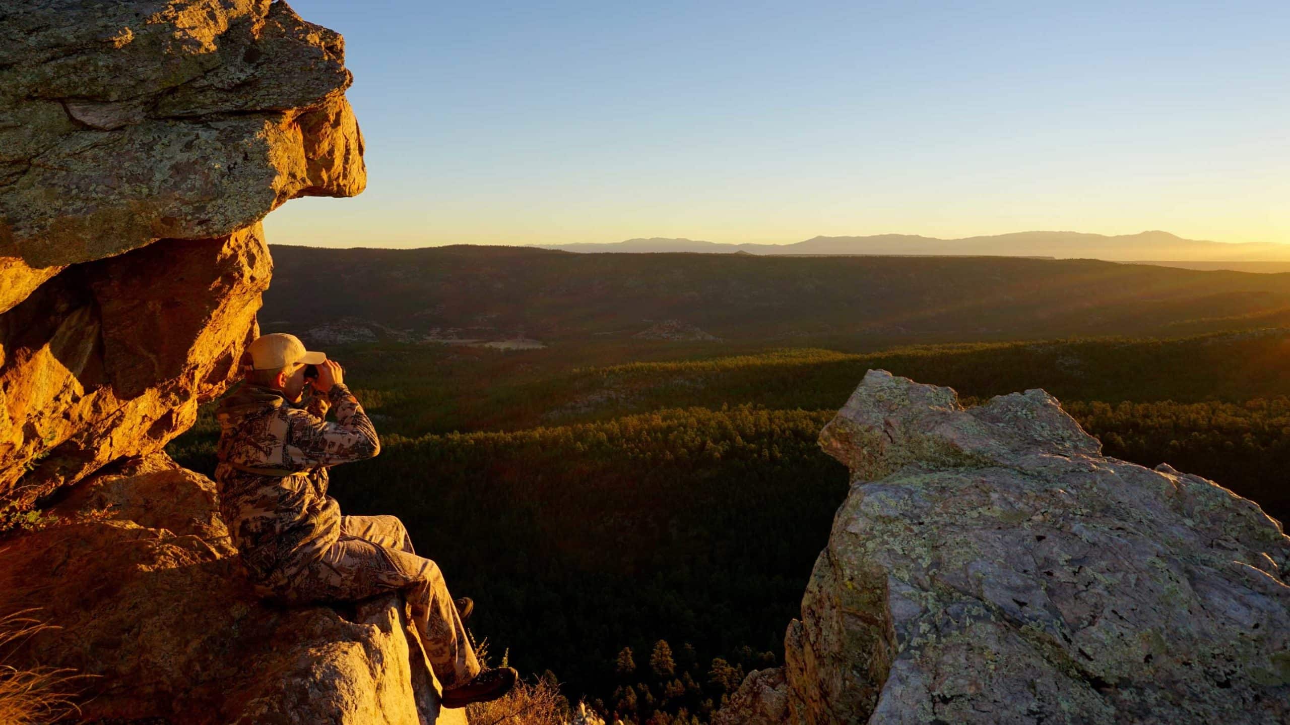 Image of hunter watching the sunset from a rocky mountainside in public lands.