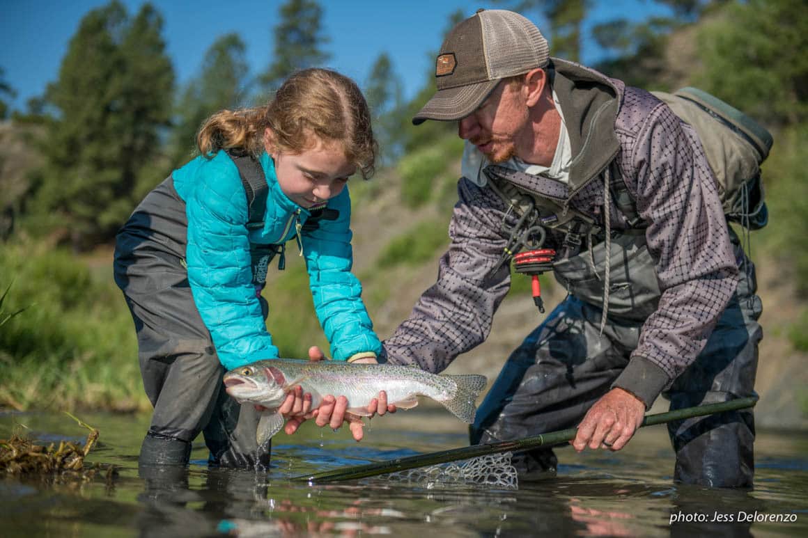 Father and daughter netting trout while fishing in a river.