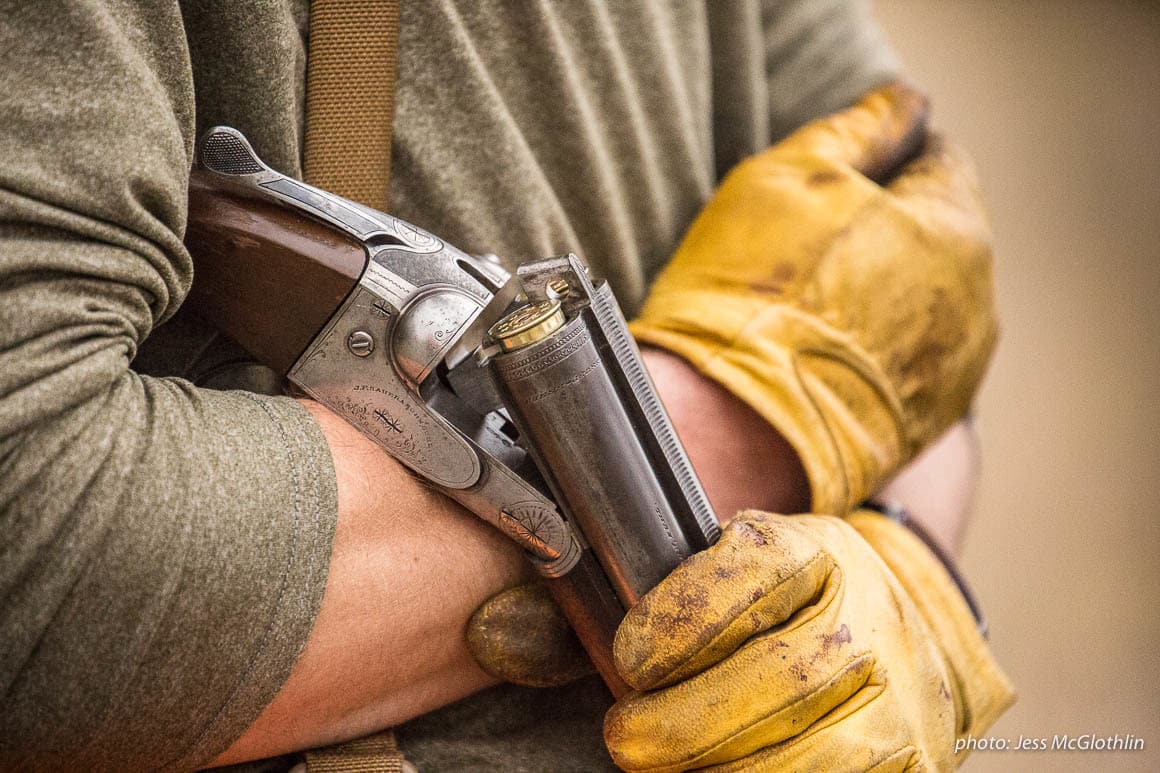 Details of a shotgun, strap vest and worn leather gloves on a hunter while upland bird hunting in eastern Montana.