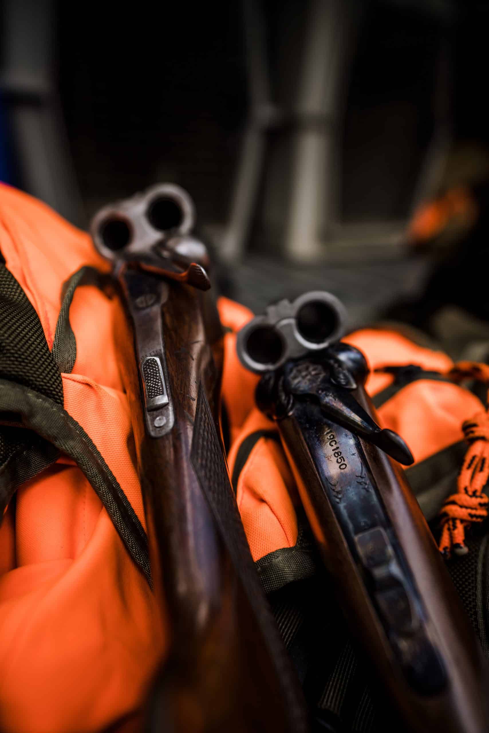 Two side-by-side shotguns rest on an orange upland vest.