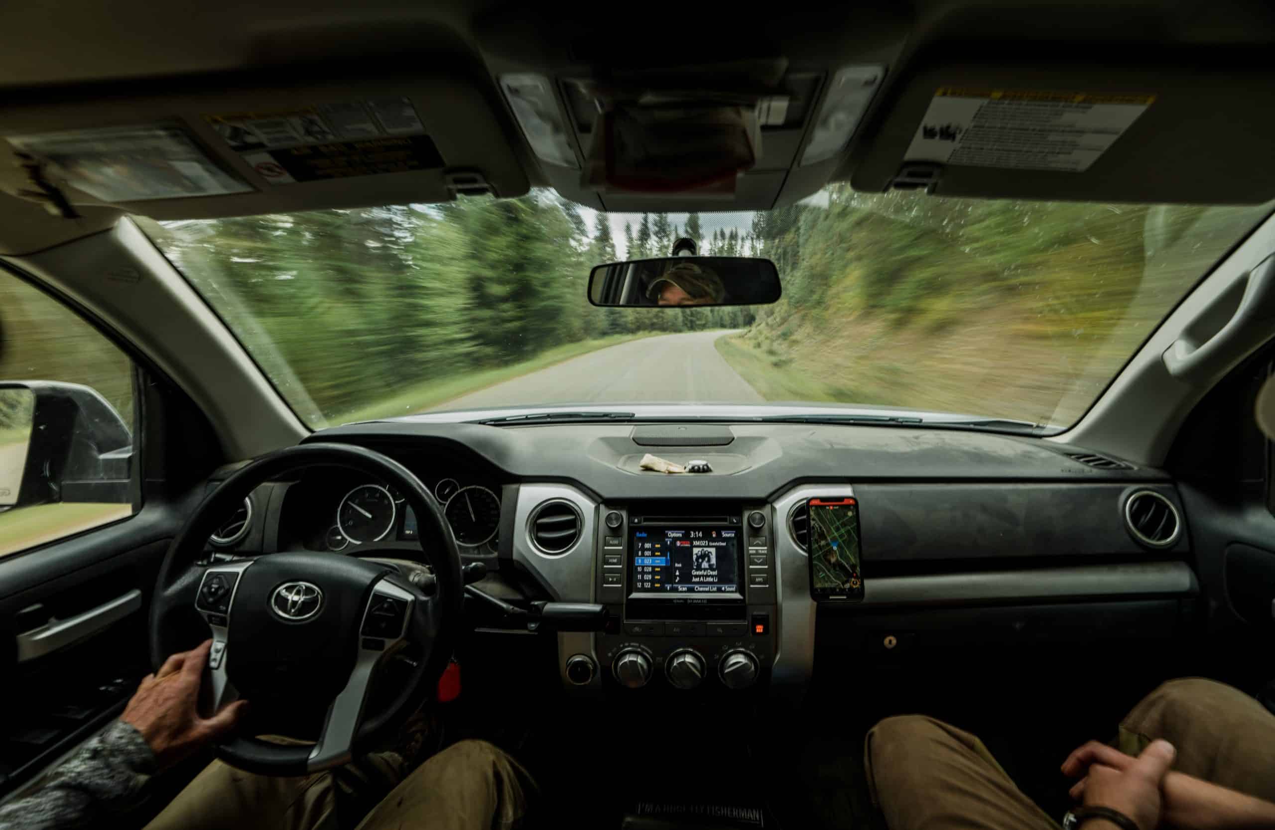 Two hunters ride in a truck while looking at the onX Hunt App.