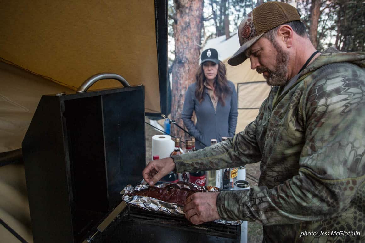 A man and woman cook food while in a wall tent camp hunting in Montana.