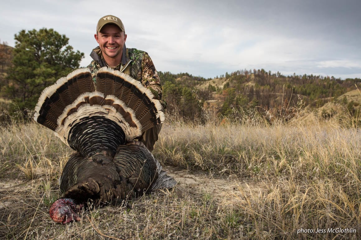 Man poses with a turkey he shot while hunting in Montana.