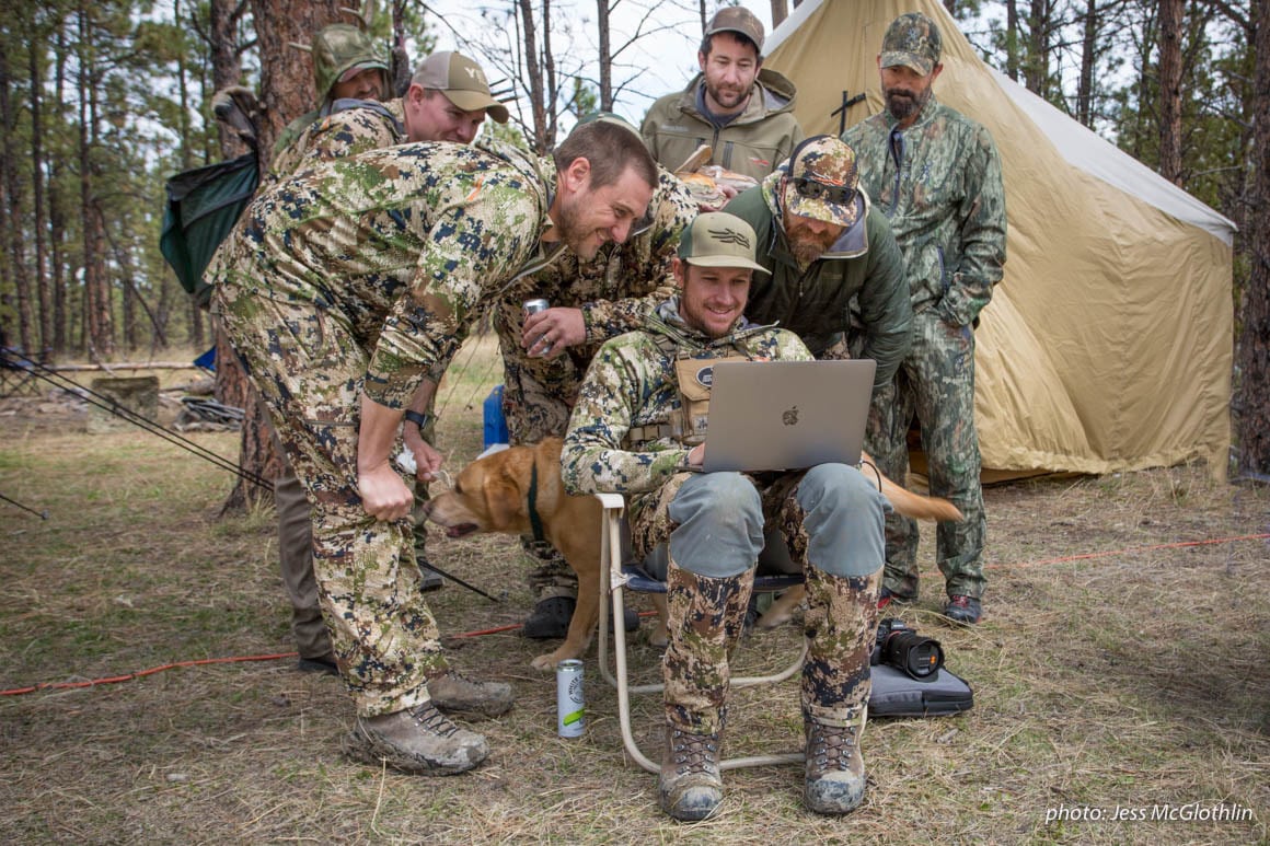 Hunters gather around a computer while in a wall tent camp in Montana.
