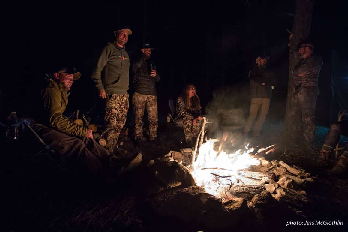 Men and women gathered around a campfire while hunting in Montana.