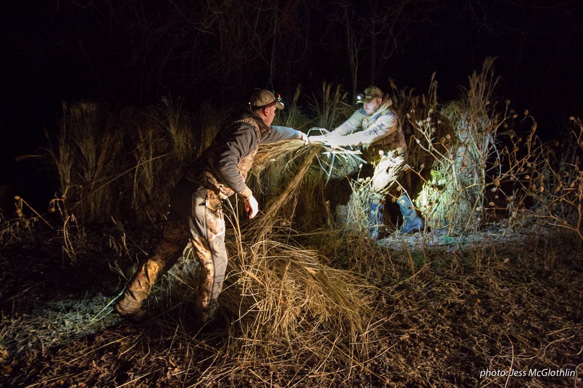 Two men work to set up a goose blind by headlamp.