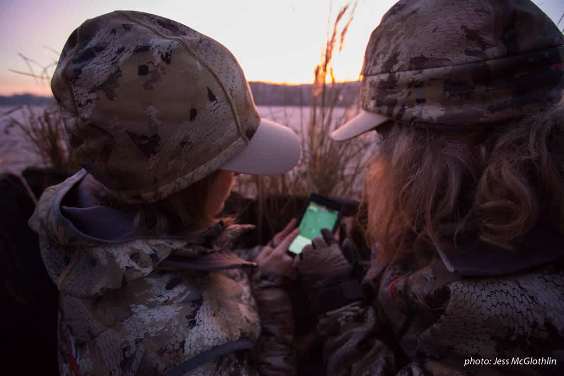 Two female hunters look at the onX Hunt App while in a goose blind at sunrise in New Jersey.