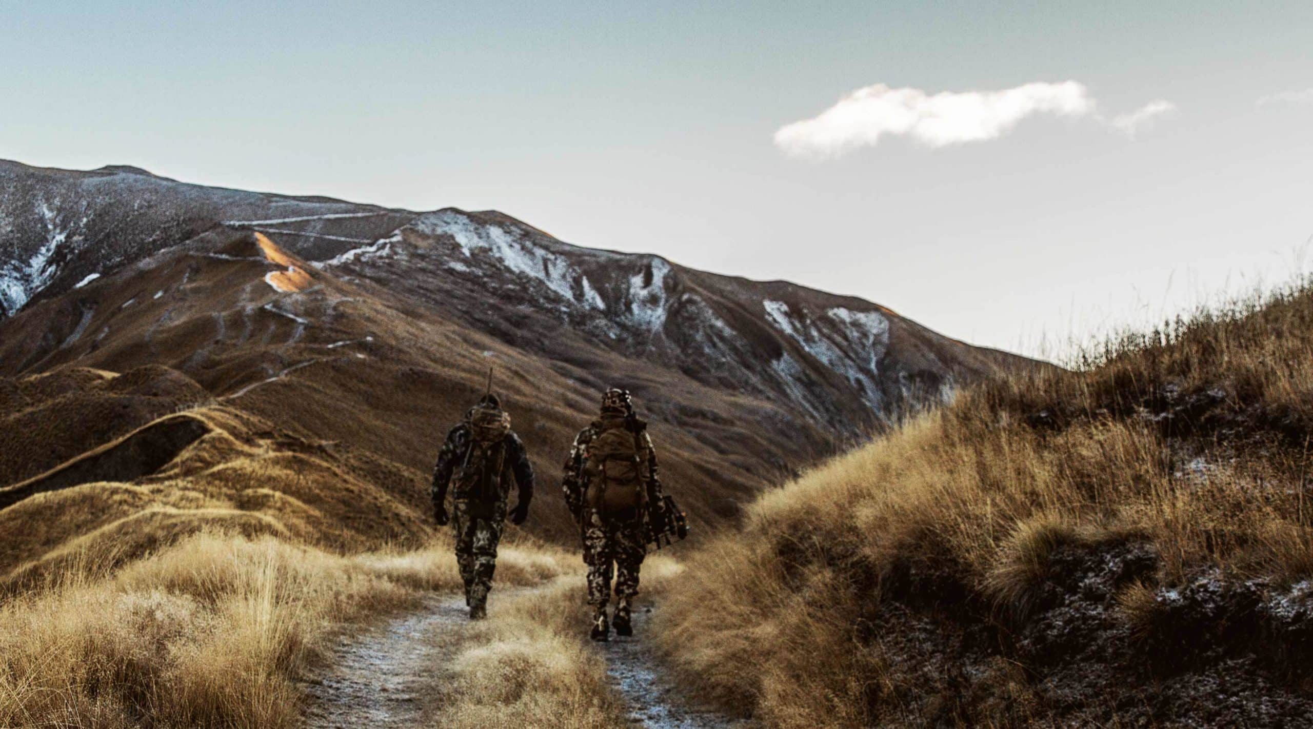 Two men in camouflage walk into the mountains in morning to hunt.
