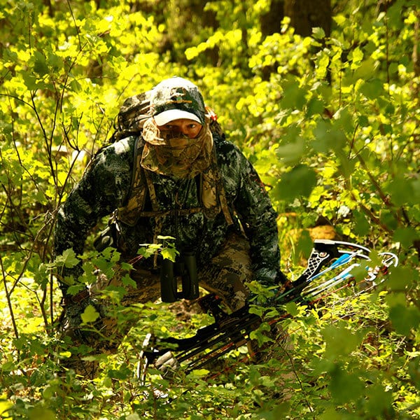 Image of hunter in full camouflage sneaking through the woods with bow in hand.