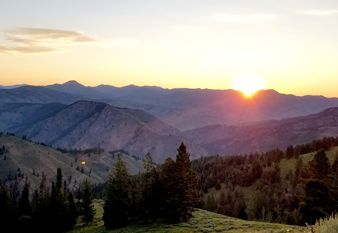 A wilderness sunset in the mountains, as the sun sets below the horizon.