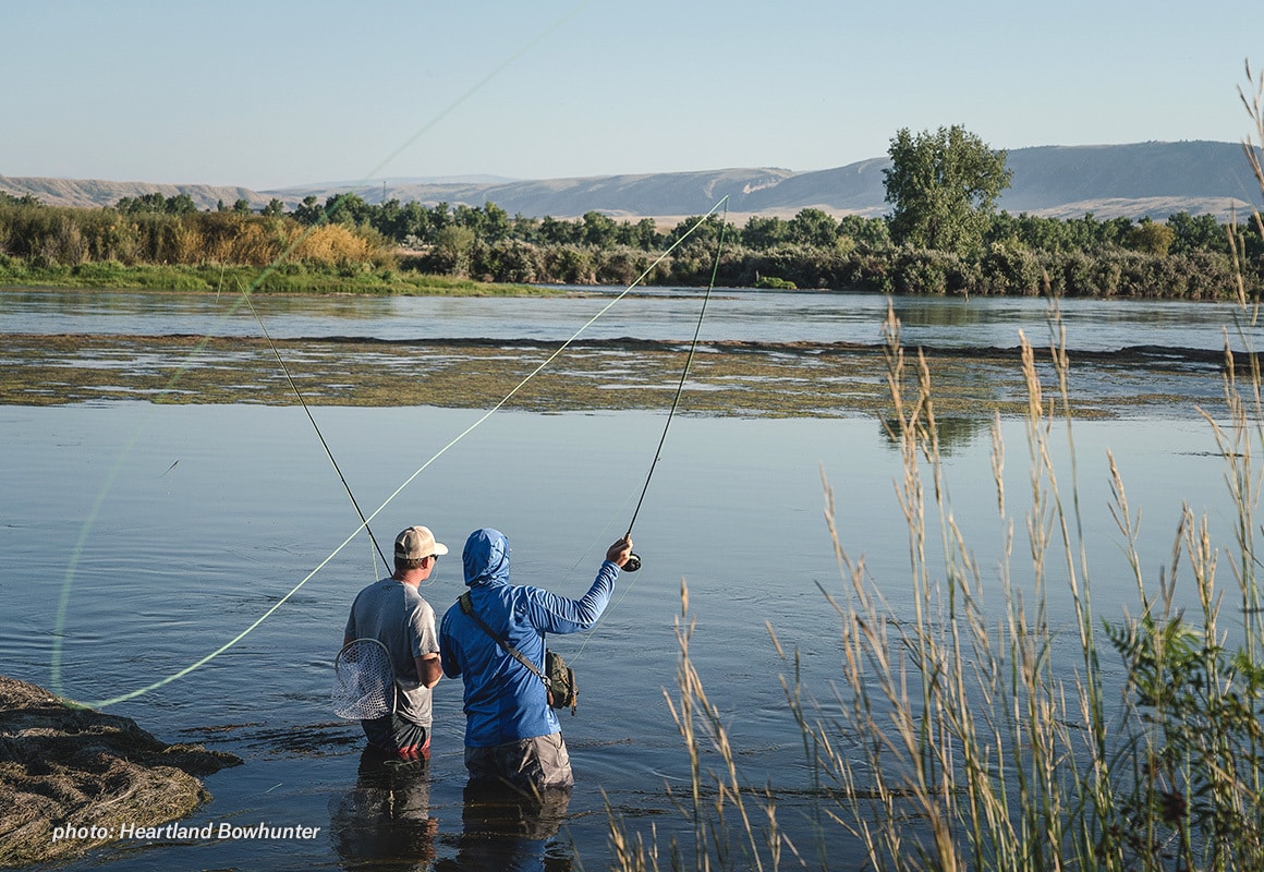 Two men fishing a river in the summertime with fly rods.