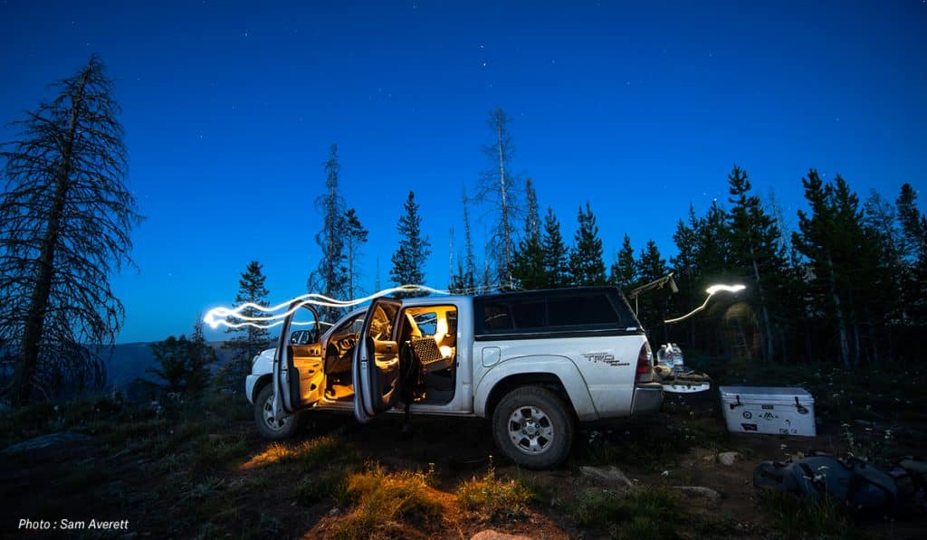 A hunter's pickup truck at parked in the woods at night.