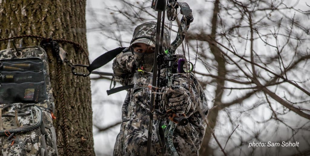 A bowhunter takes aim at an animal from a treestand. 