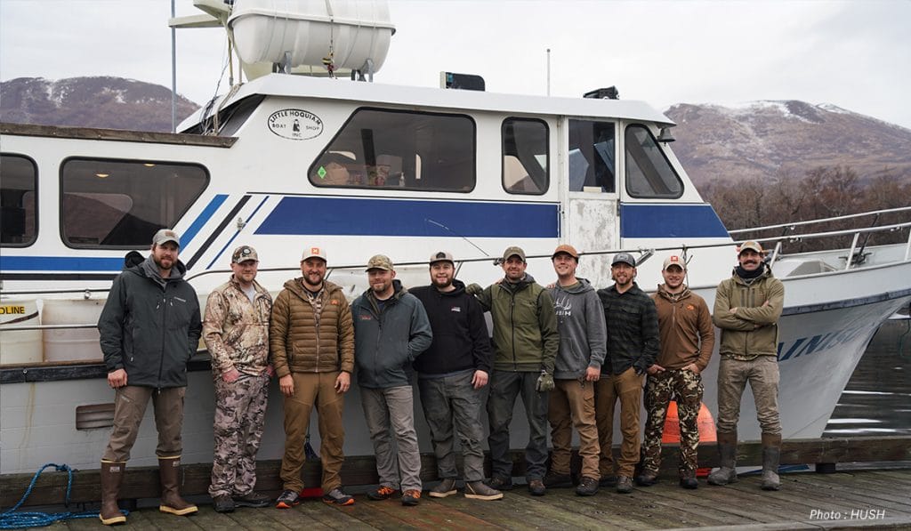 A group of 10 men pose for a photo in front of a boat. 