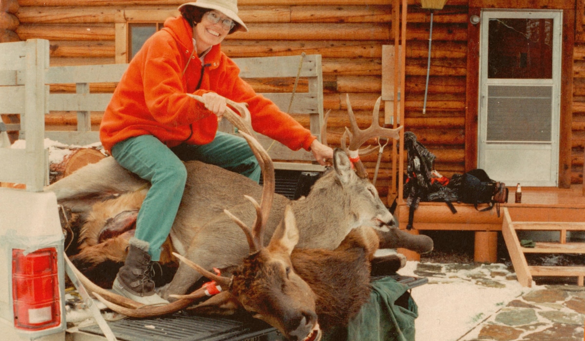 Woman hunting a bull elk and buck deer in Montana in front of a cabin.