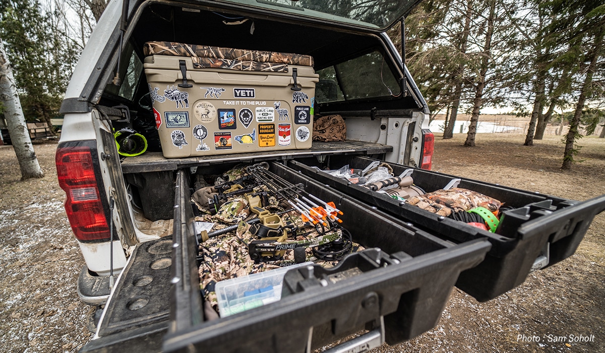 Hunter organizing the back of his truck with bow, cooler, and other gear.