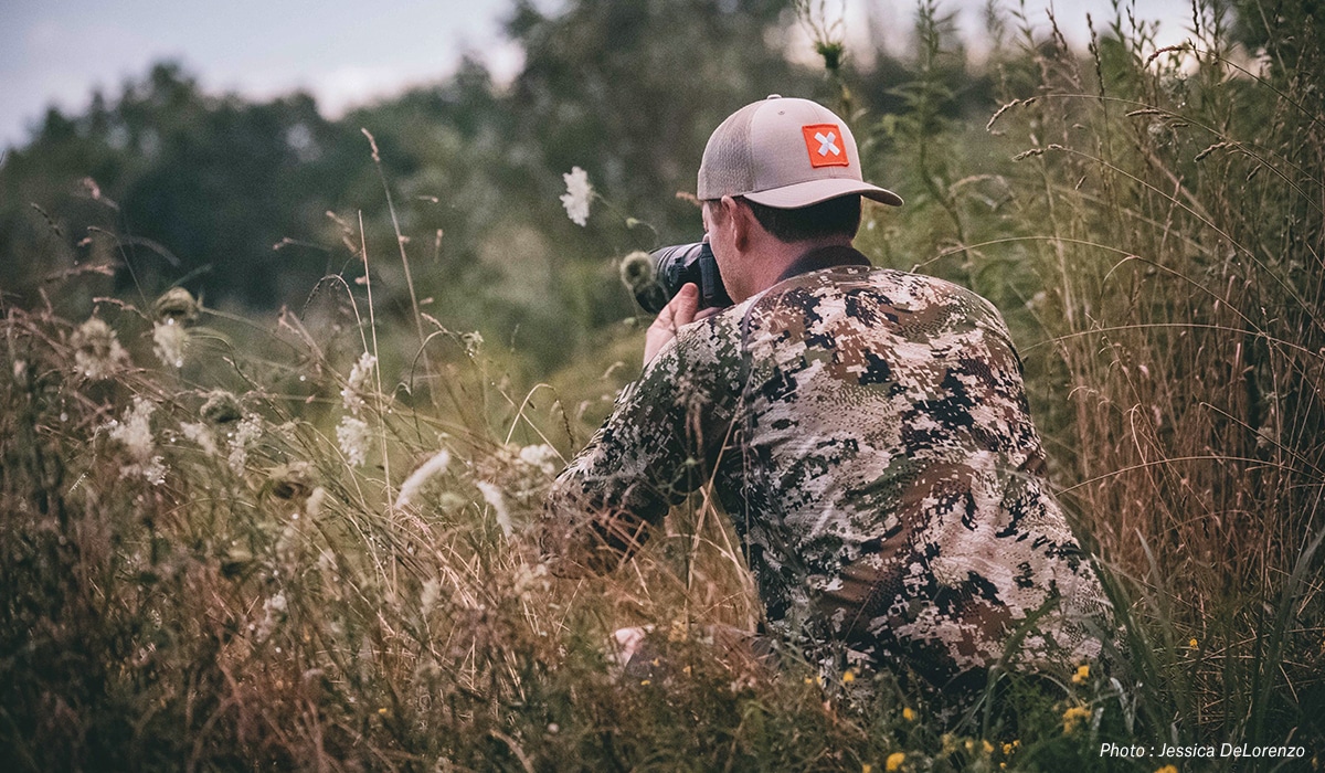 A man in camouflage with a camera in the field.