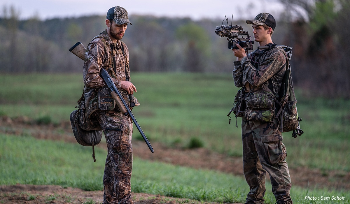 Two hunters, one with gun and one with video camera.