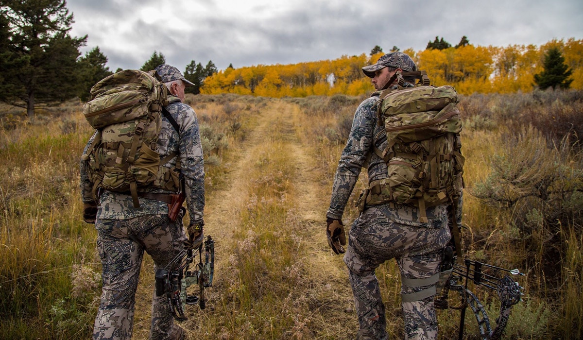 2 hunters in camo and backpacks walking up a hill