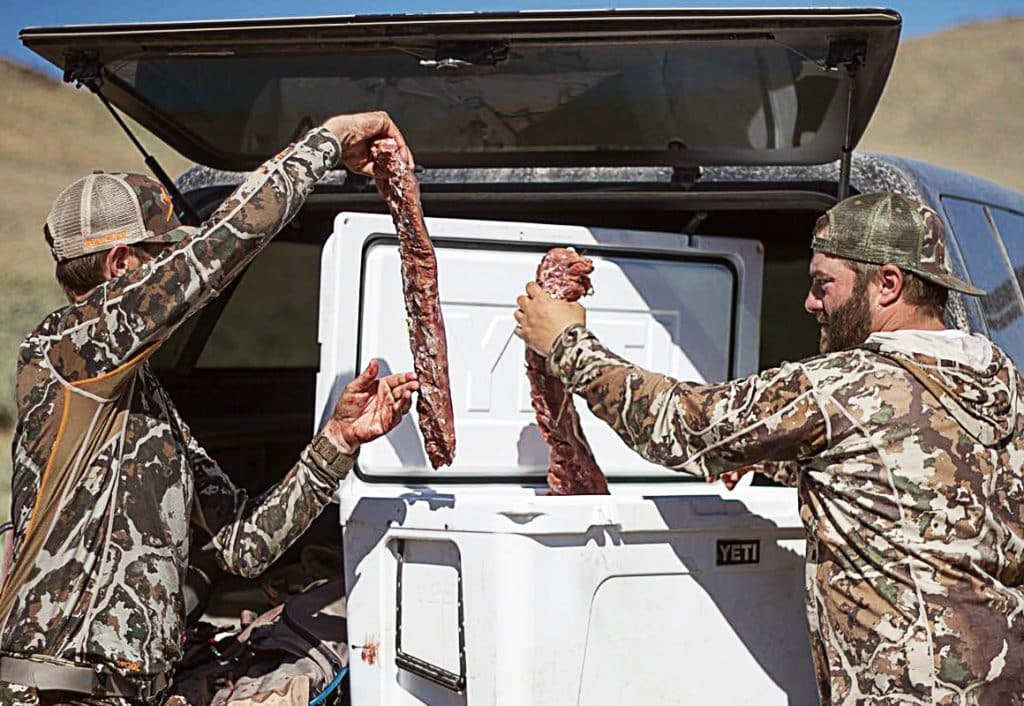 Two hunters hold backstraps out of a cooler.
