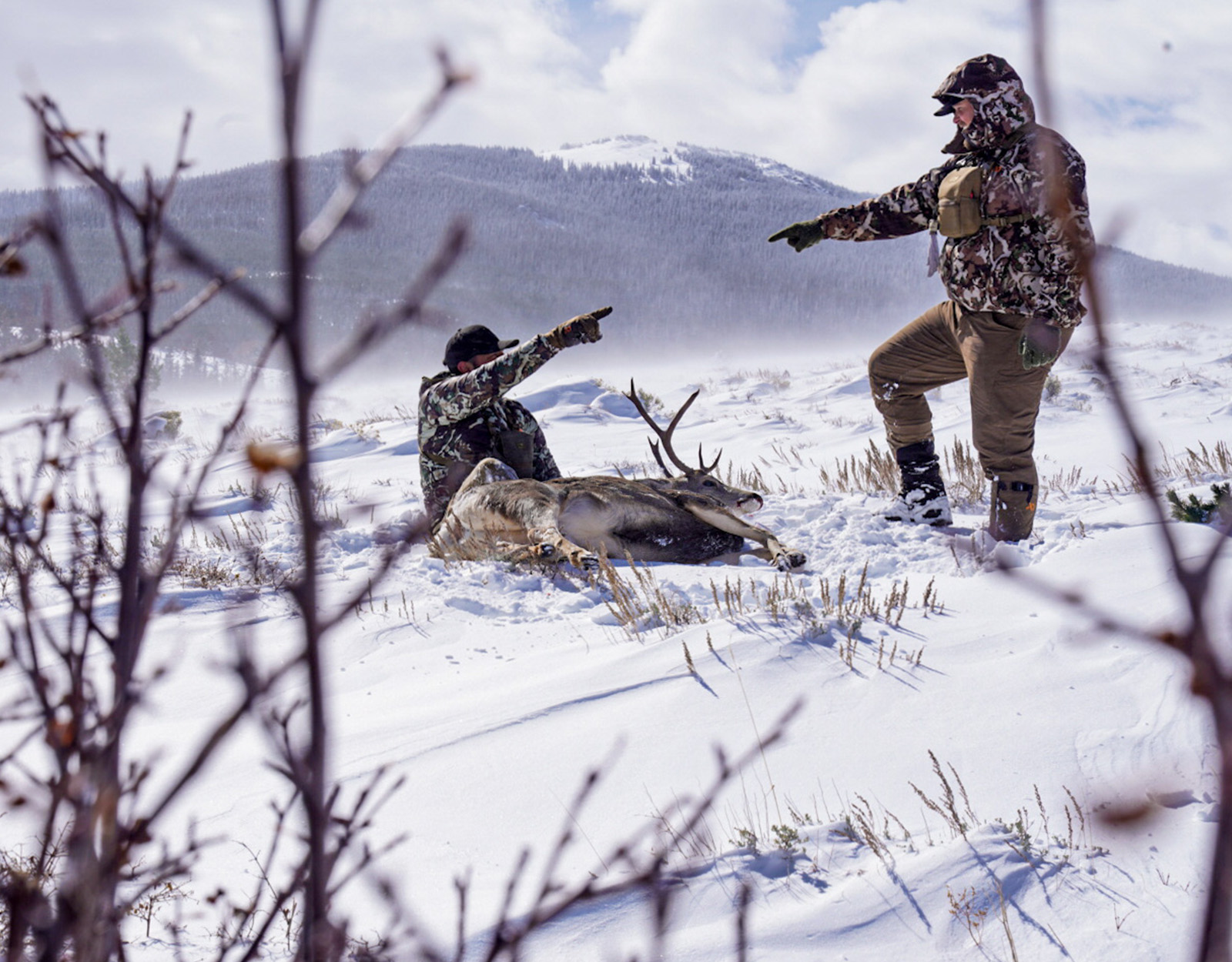 Two hunters celebrate harvesting a deer in the snow. 