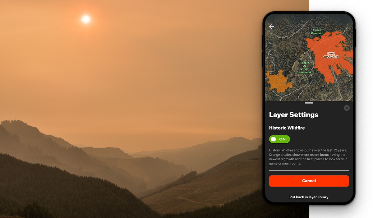 A mountain landscape covered in the orange haze of wildfire smoke. A screenshot of the onX Hunt App is overlaid on the photo showing "Layer Settings."
