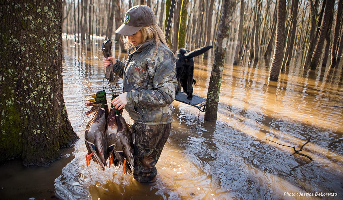 A female waterfowl hunter walks through a wetland.