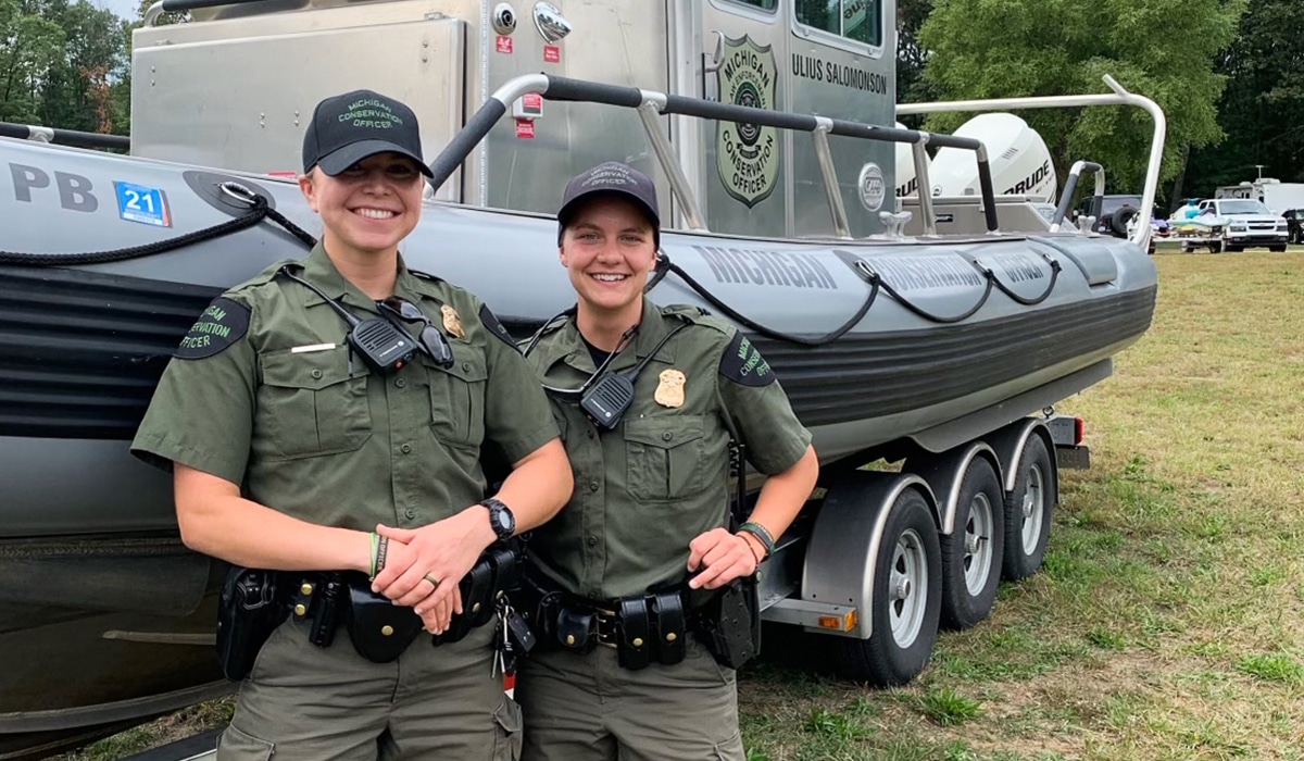 Two female game wardens pose for a photo in front of a boat.