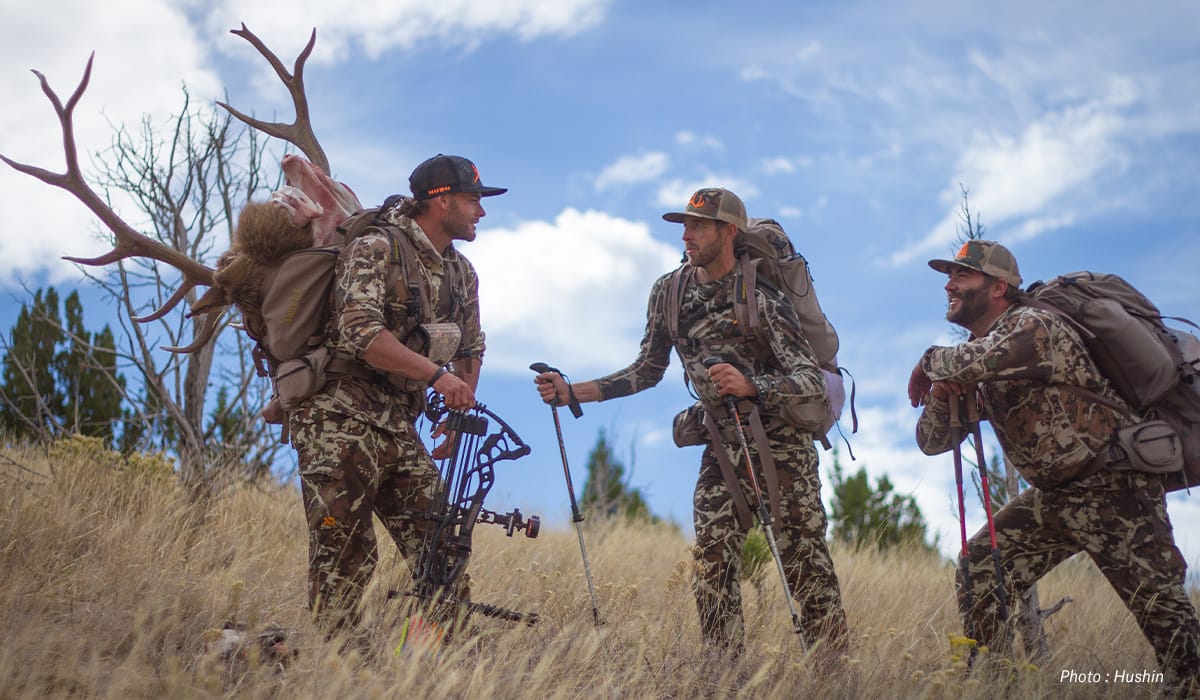 3 hunters in camo with antlers on their back in a field 