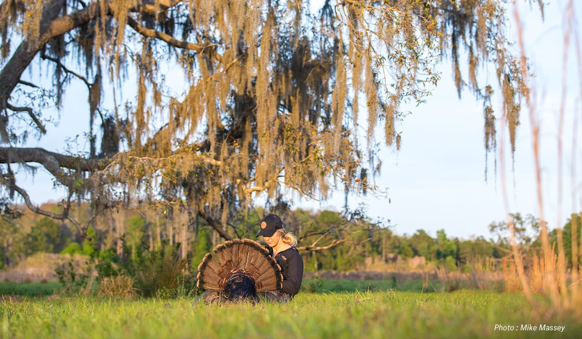 a female hunter in a field with a downed turkey in the best state to hunt turkey, Texas