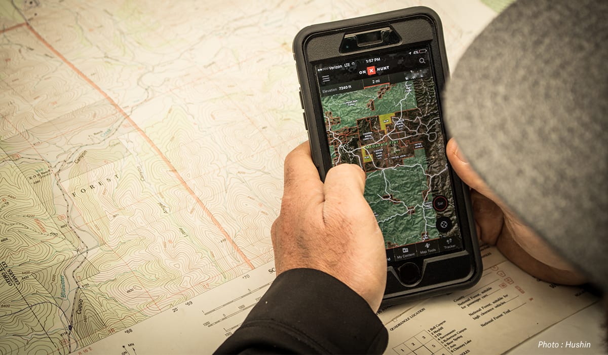 A close-up of hands holding a mobile phone with the onX Hunt App on the screen.