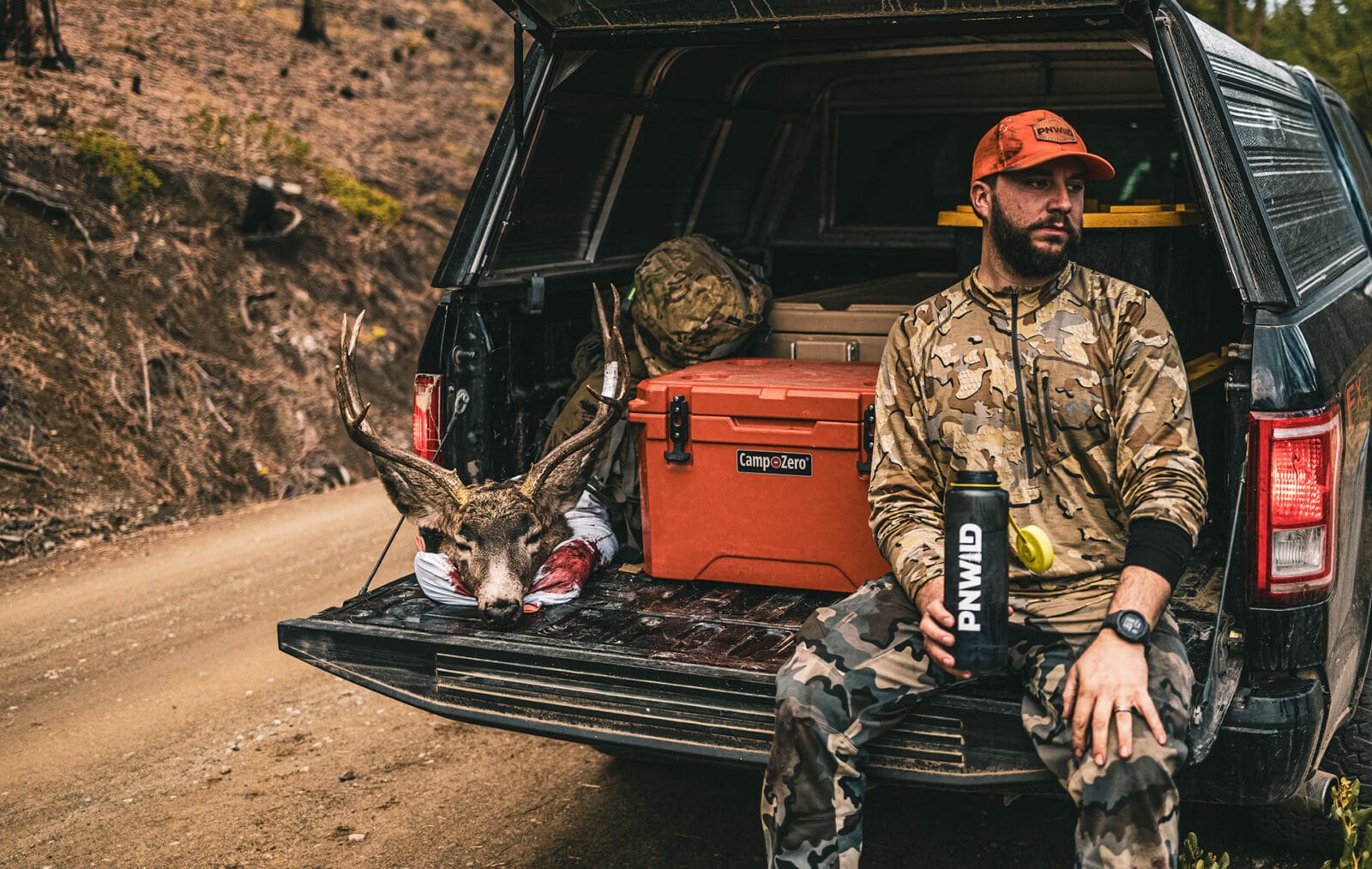 A hunter wearing camo sits on his tailgate after a successful deer hunt.