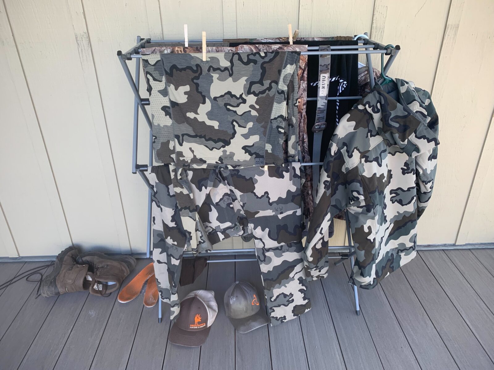 Hunting clothing hangs from a clothing rack to air dry on a porch. 