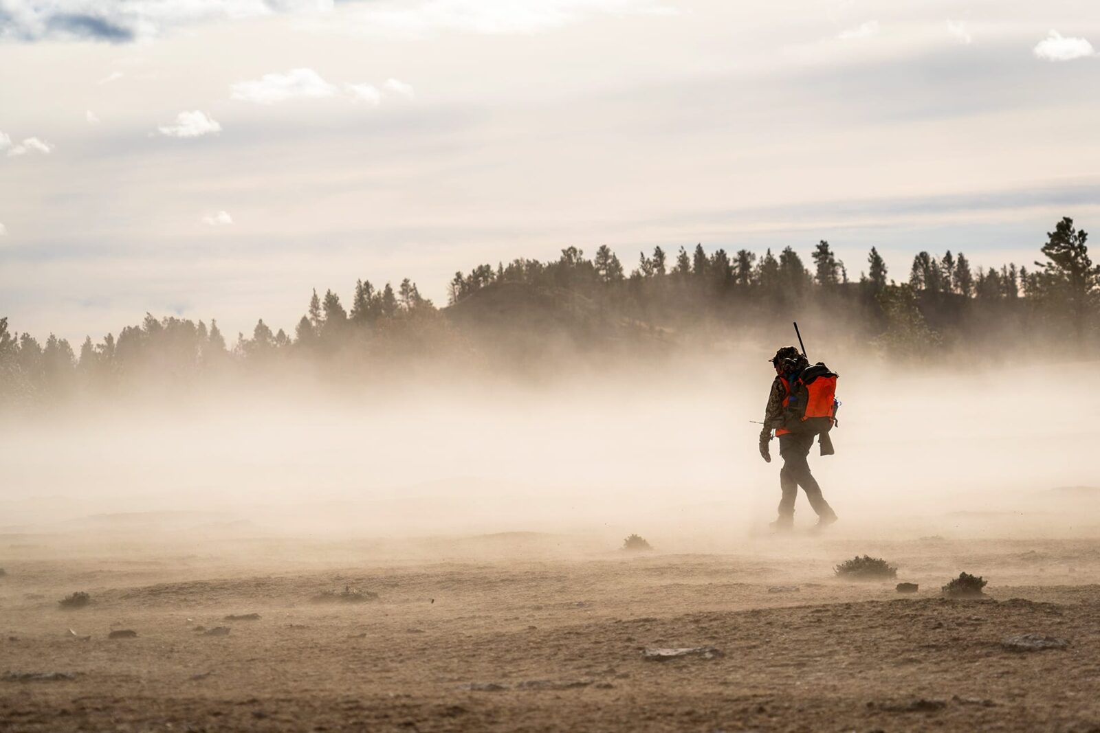 Hunter in hunter's orange with a rifle walking through mist to find a mule deer 