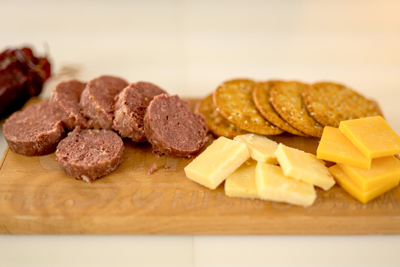 Summer sausage on a charcuterie board alongside slices of cheese and crackers.