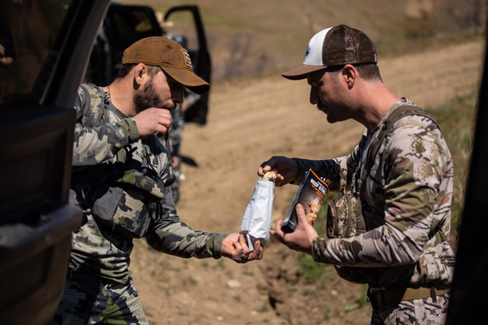 Two hunters take a meal break back at their trucks. One hunter is letting the other try his Peak Refuel meal. 