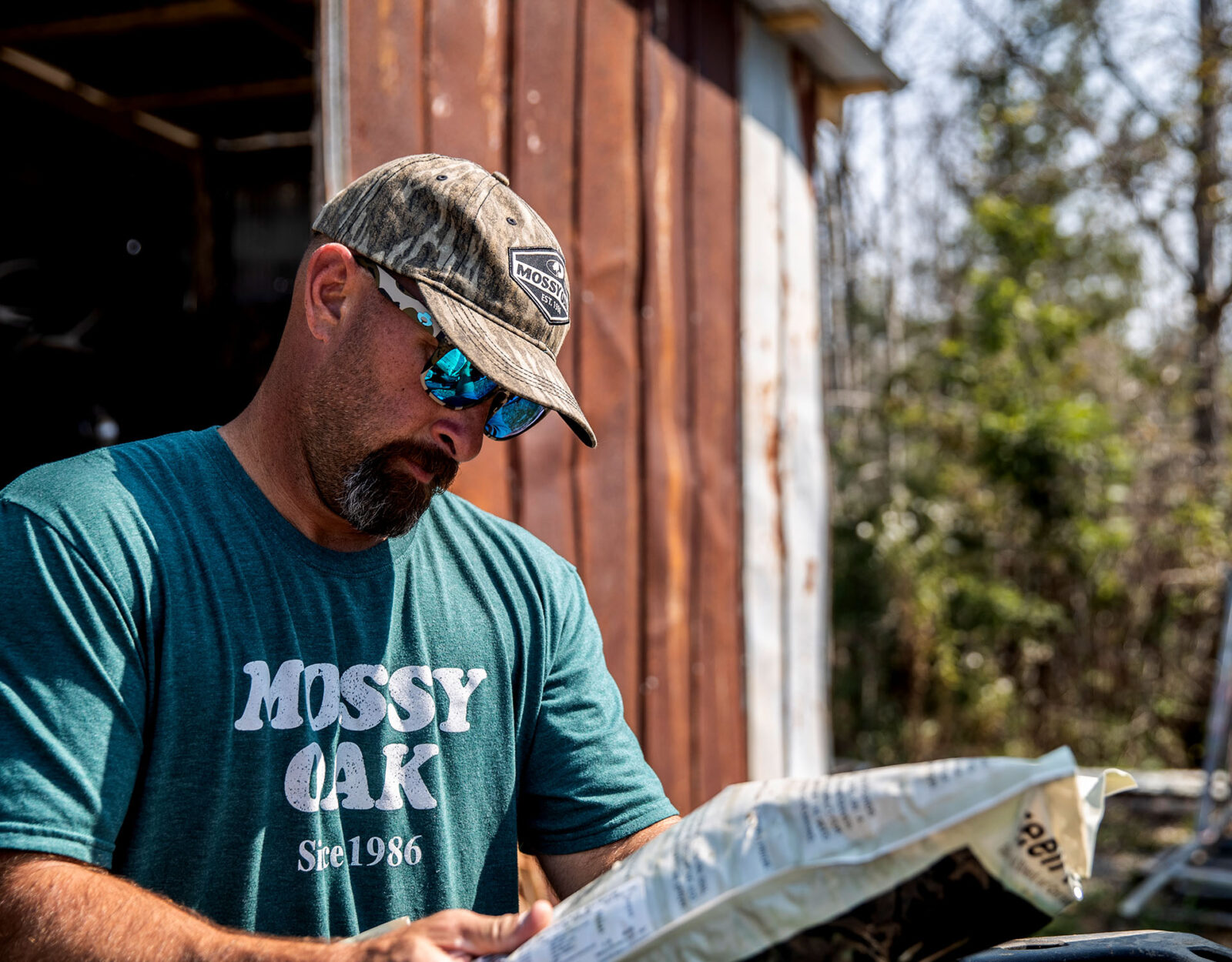 A man in a Mossy Oak tshirt reads the packaging of a seed bag. 