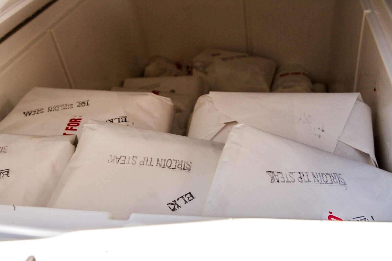 Processed game meat packaged in white parchment paper and stacked in a chest freezer.