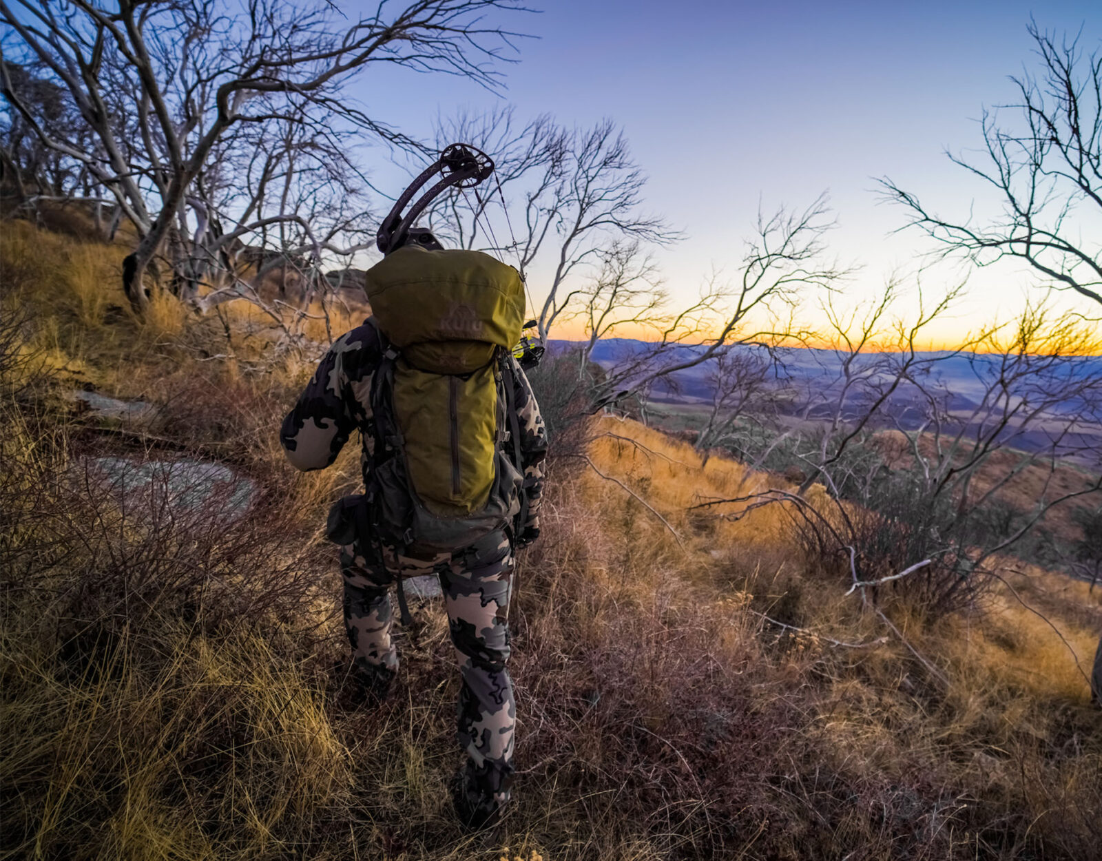 A bowhunter wearing a pack sidehills through the mountains. 