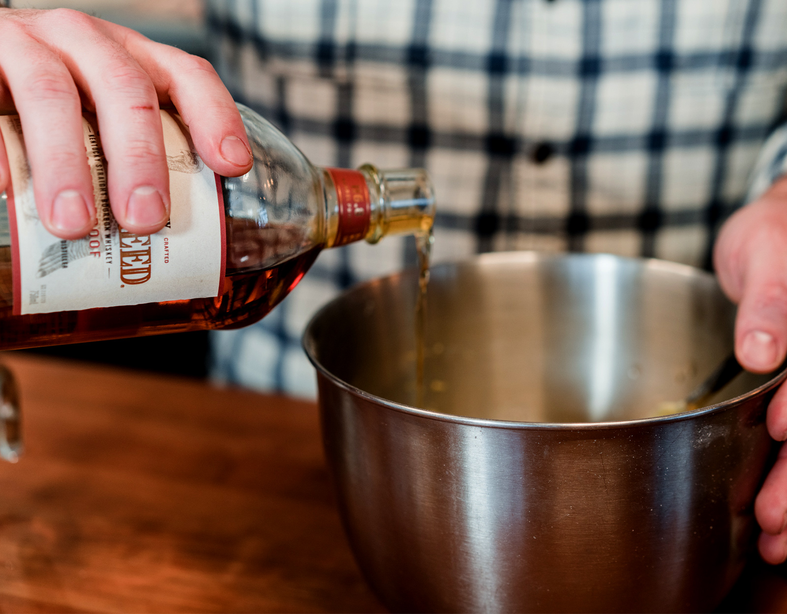 A person pours bourbon into a mixing bowl for baking. 