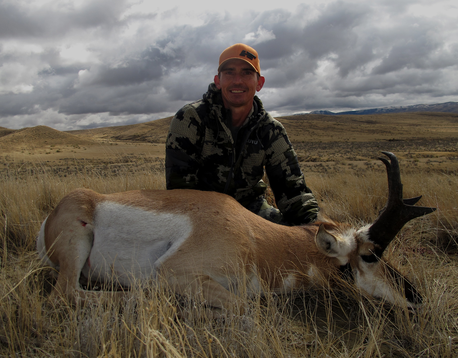 A hunter poses with the pronghorn he harvested. Rolling grasslands are in the background.