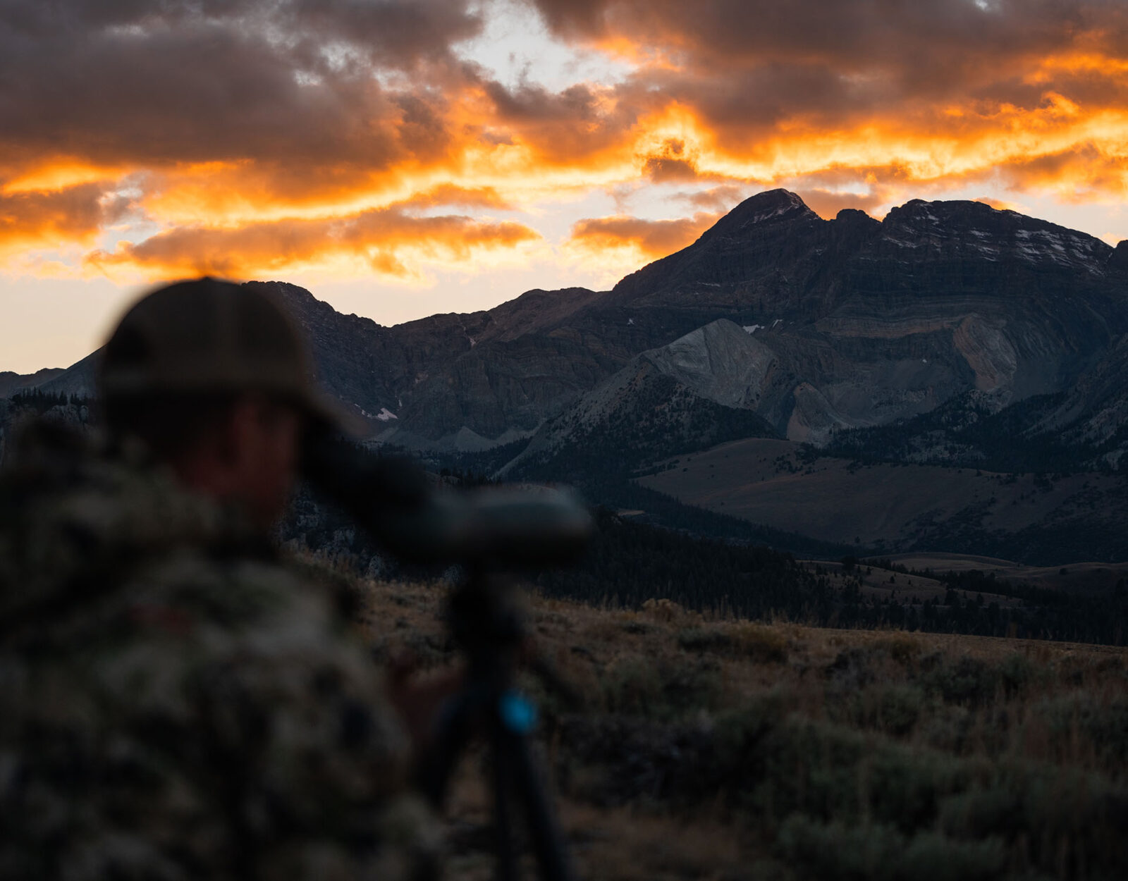 Man glassing while hunting in front of mountains at sunset