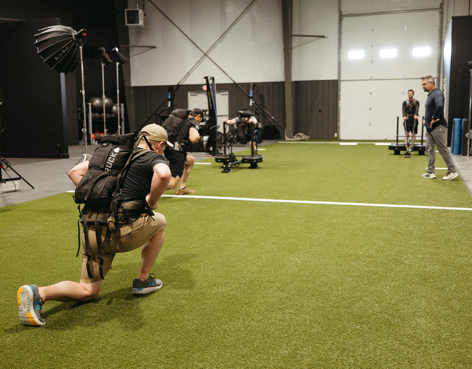 Two men performing walking lunges wearing ruck sacks in a crossfit gym. 