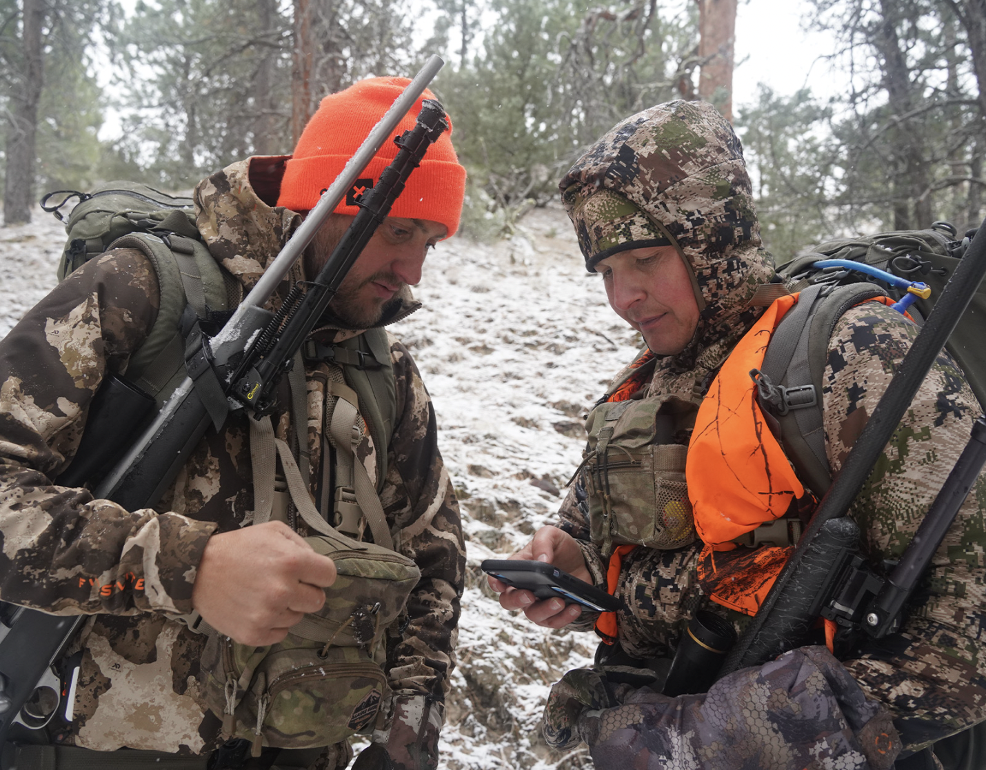 two hunters in camo looking at a hunting gps app on their phone 