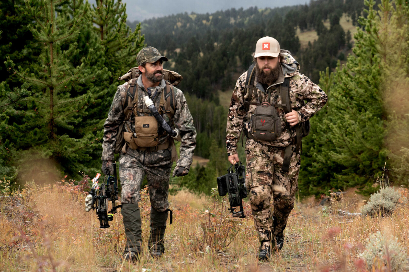 two hunters walking in the woods with compound bows