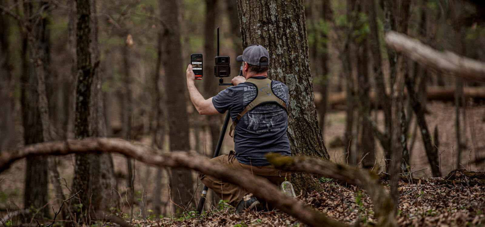 an eastern hunter in the woods looking at his trail camera data on his phone through onx hunt